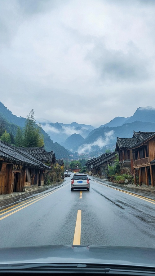 汽车视角，前面有汽车，在宽阔的马路上一路向前，远处的山峰云雾缭绕，仙气飘飘，景色宜人，山脚下有木屋栋栋，炊烟袅袅