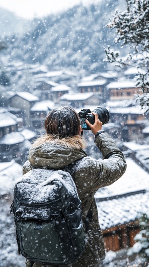 短发女摄影师在雪景中拍摄村庄与树木