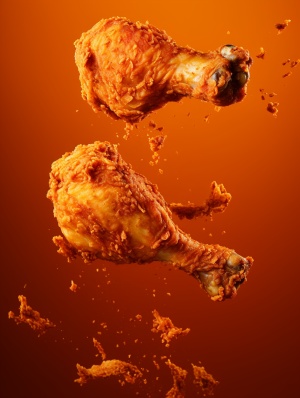 Crispy chicken legs in the air, The skin of crispy fried chicken legs scattered in the air, Yellow and red style，There's a little paprika on the chicken leg，Warm yellow background , Wide Angle, close-up,Focal length 55mm，Aperture f1.9，photo-realistic still life, Soft box lighting，Desktop photography